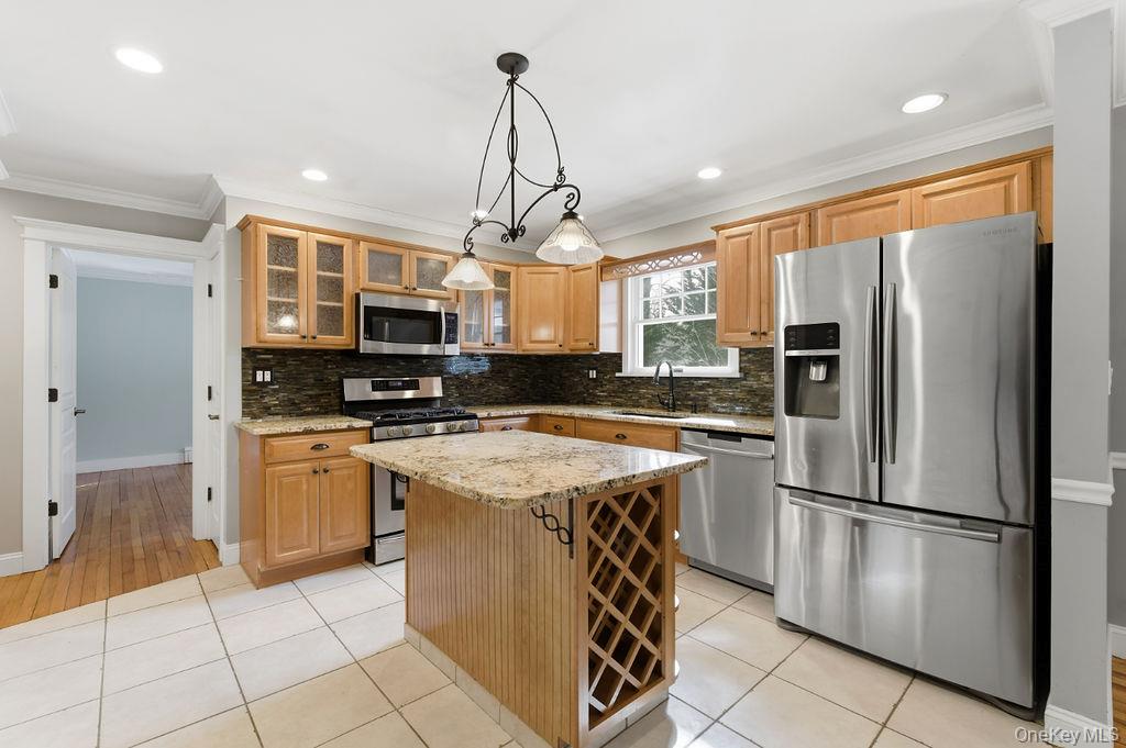 Kitchen with honey-colored cabinets, stainless steel appliances, and a granite island with a wine rack.
