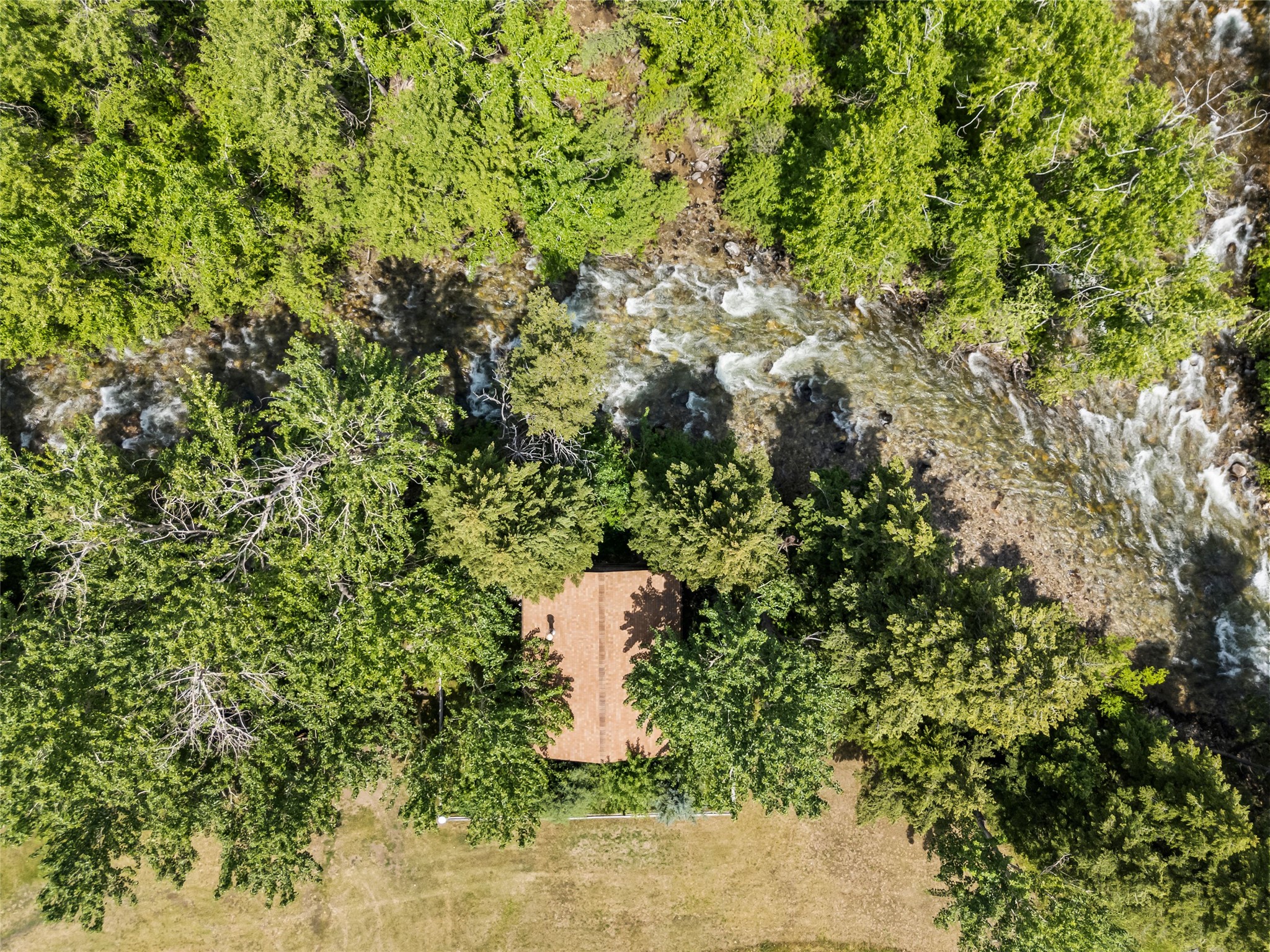 Aerial view of a tree-surrounded home beside a rocky, rushing creek.