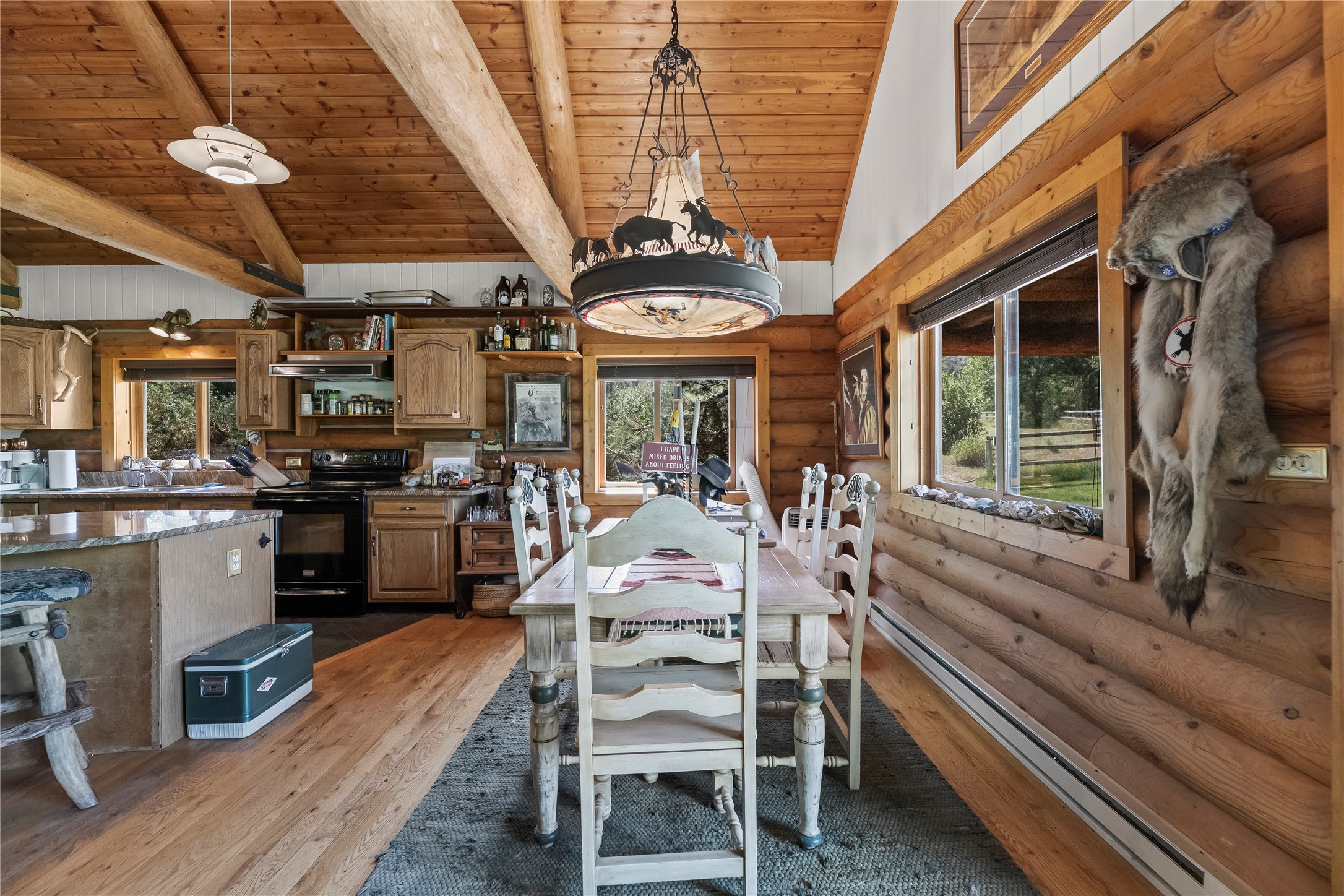 Rustic log-home kitchen and dining area with exposed beams, a white dining set, and large windows.