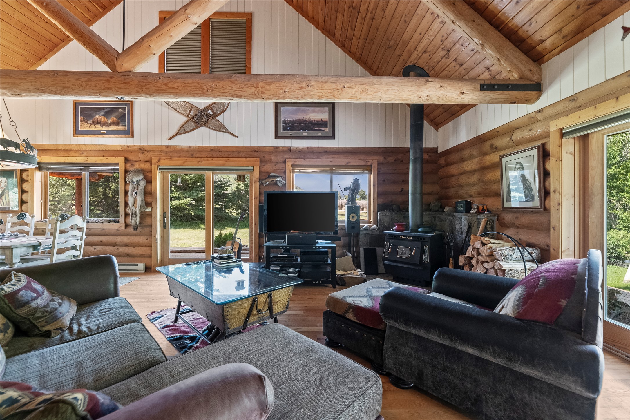 Log-cabin living room with exposed timber beams, a wood stove, and large windows.