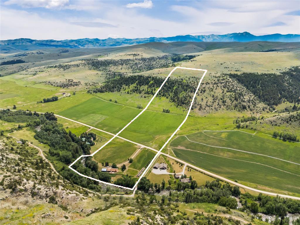 Aerial view of a rural parcel outlined in white among green fields, wooded hills, and distant mountains.
