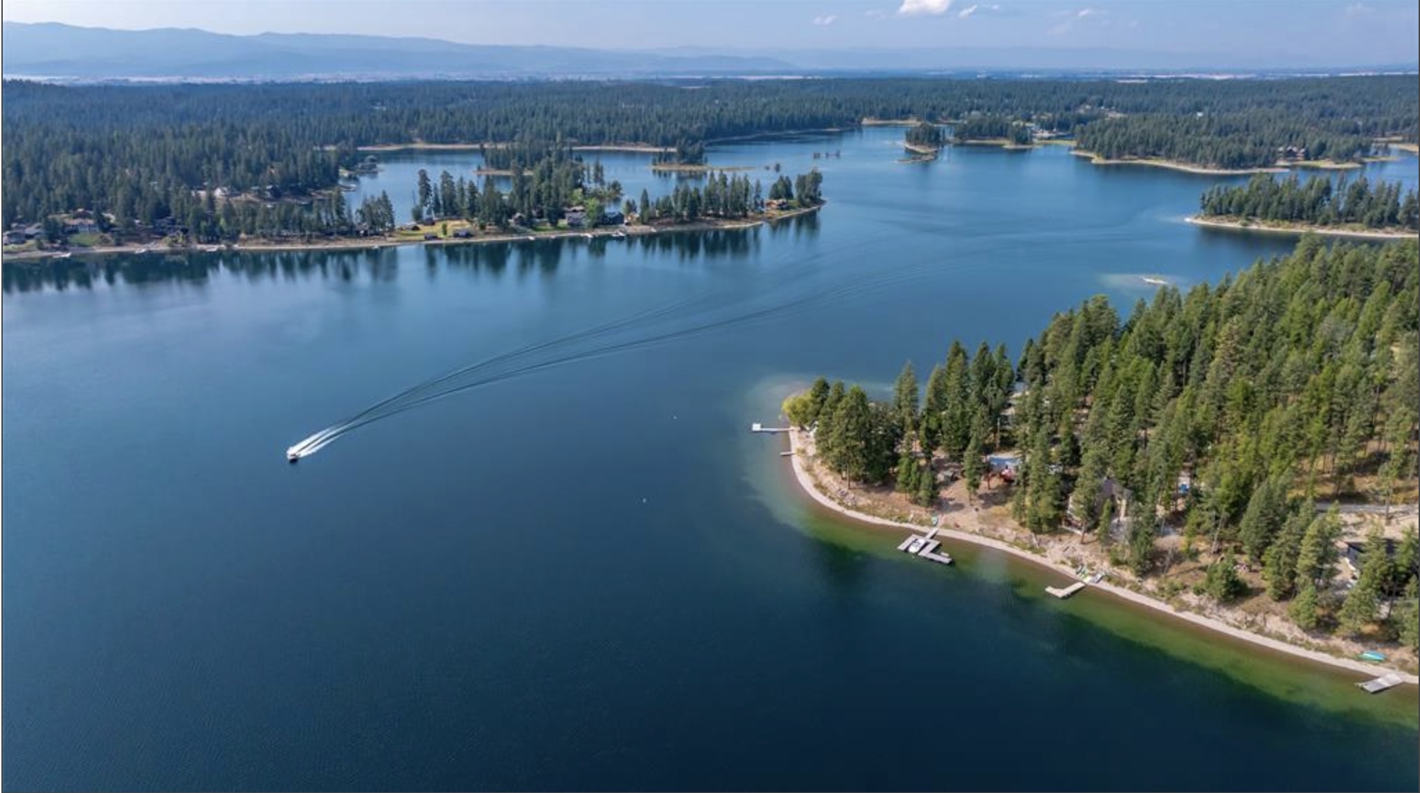Aerial lake view with forested shorelines, docks, and a boat leaving a wake.