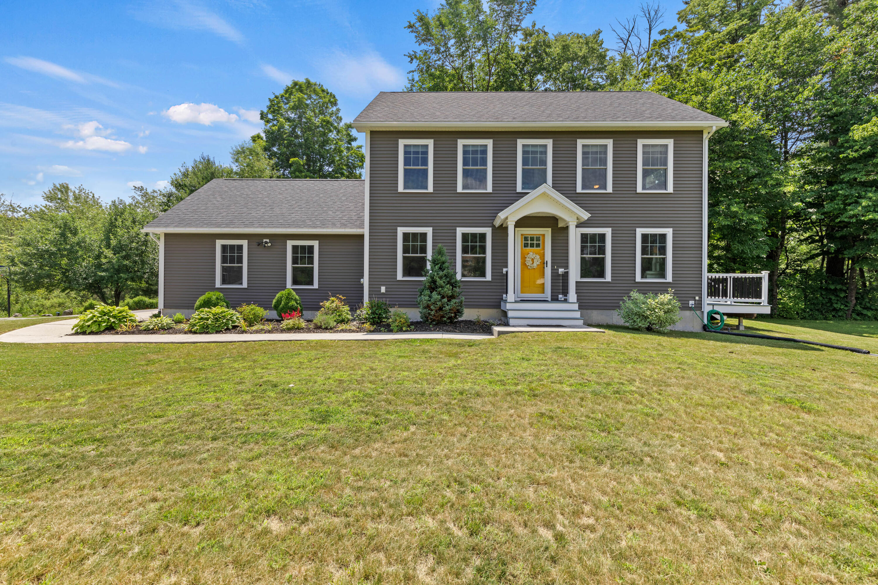 Two-story gray house with a yellow front door, landscaped beds, broad lawn, and mature trees.