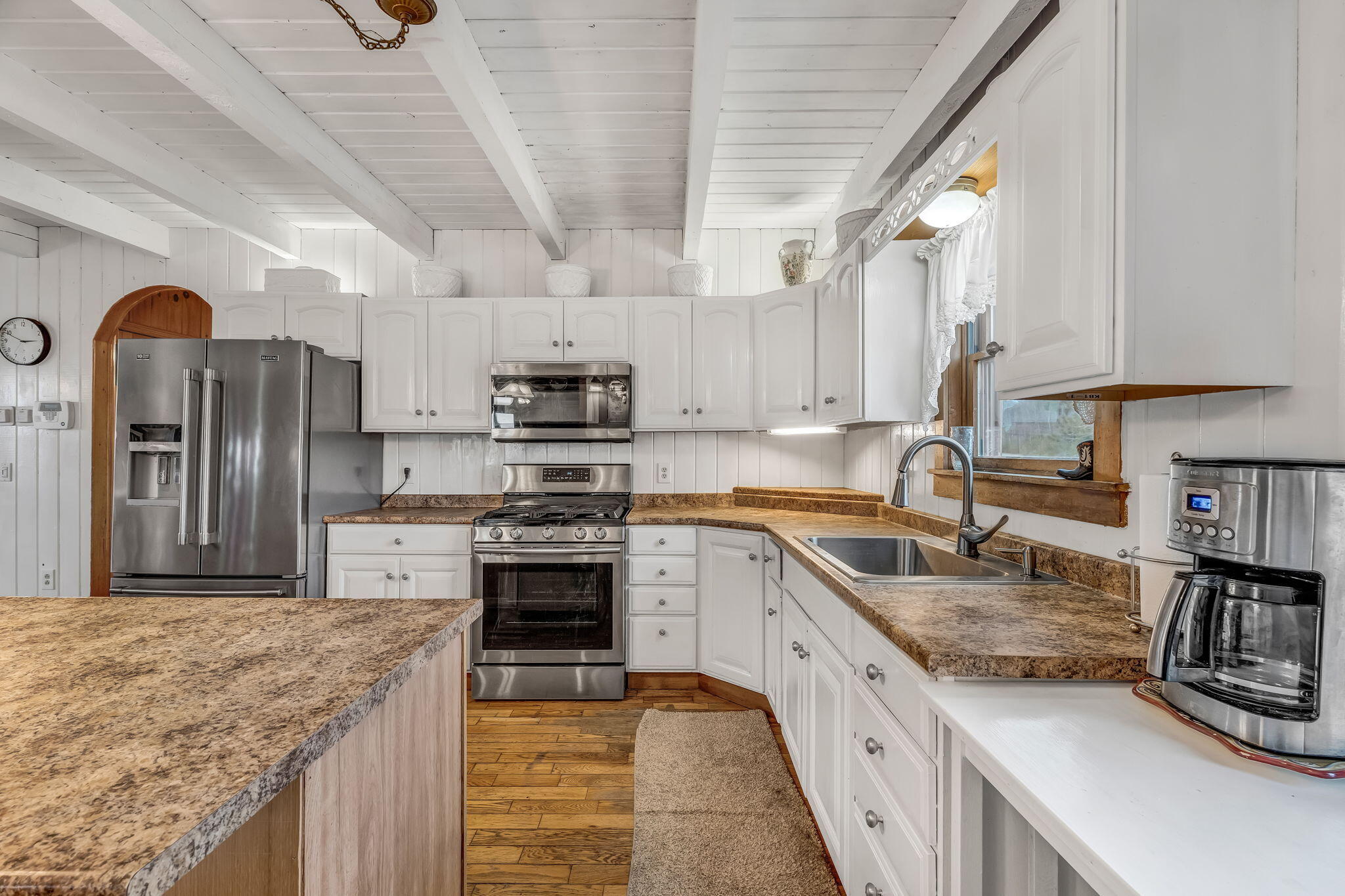 Kitchen with white cabinetry, exposed ceiling beams, granite counters, and stainless steel appliances.