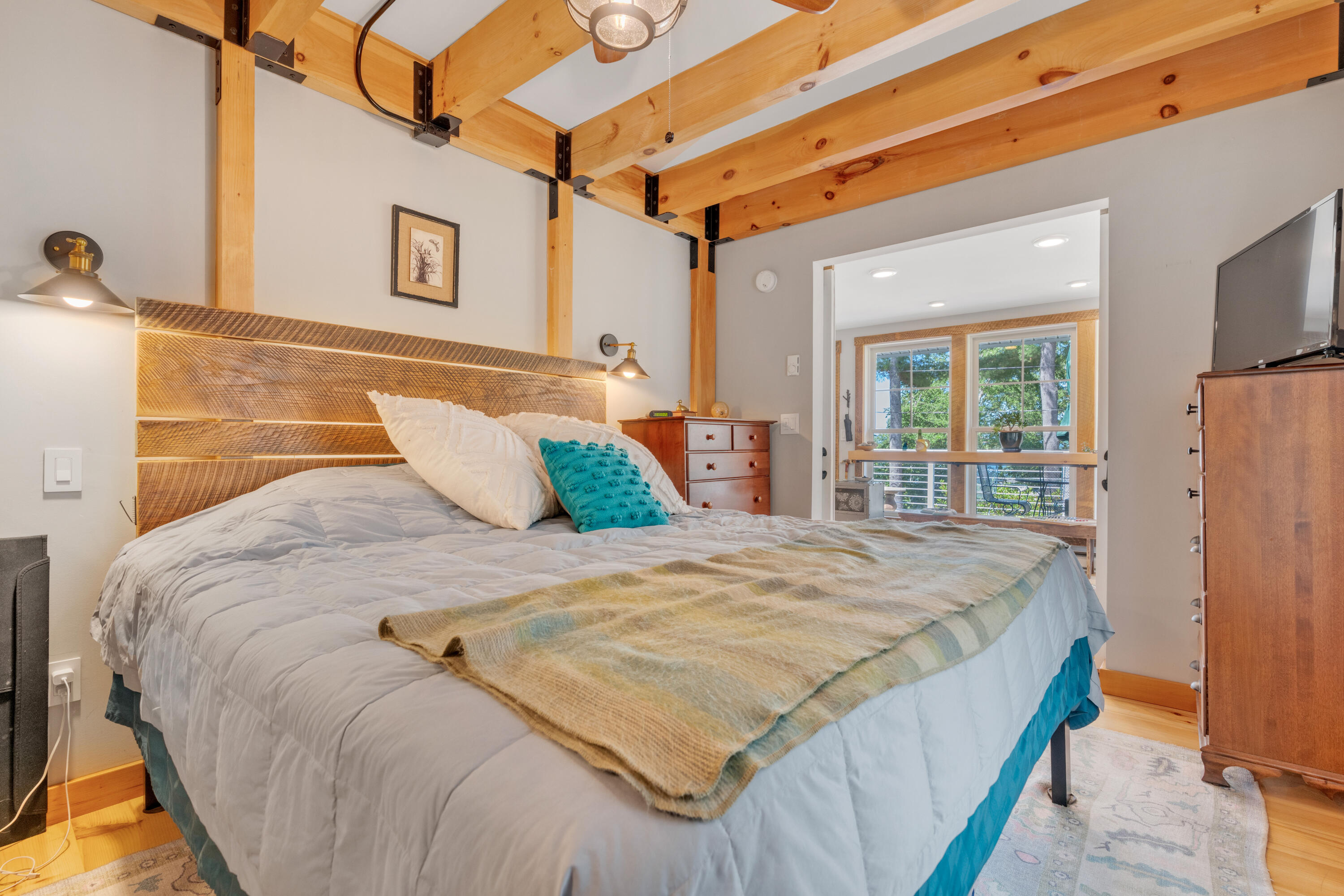 Bedroom with exposed timber ceiling beams, a wide bed, and a bright adjoining sitting area.