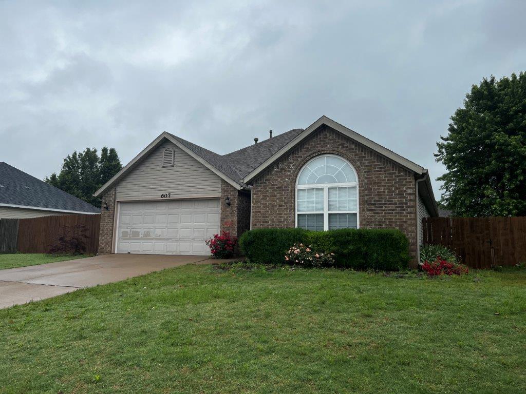 Single-story brick-and-siding house with an attached garage, arched front window, and flower beds.