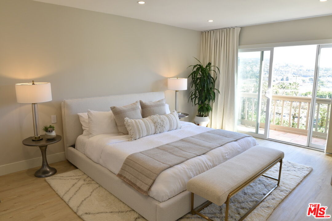 Staged bedroom with a white bed, upholstered bench, and sliding doors to a balcony.