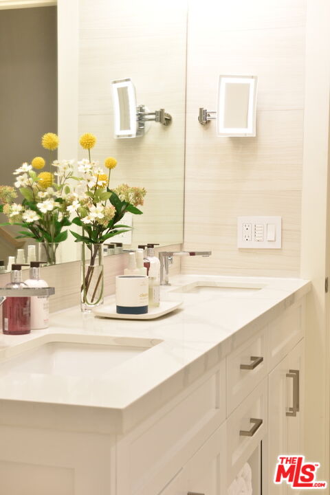 Bathroom vanity with a white countertop, mirrored wall, and vase of yellow and white flowers.