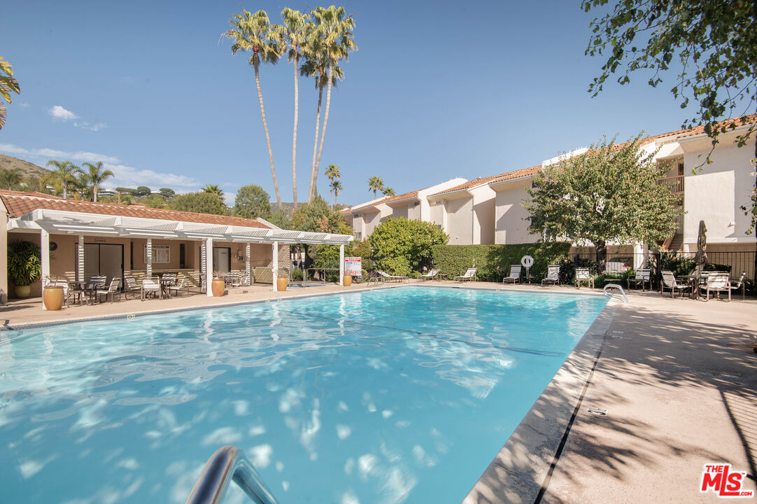 Community swimming pool beside residences, with patio seating and palm trees.