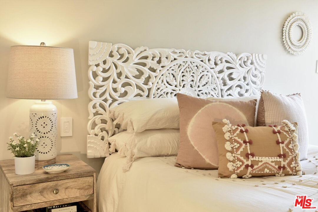 Bedroom with an ornate white carved headboard, cream bedding, and blush accent pillows.