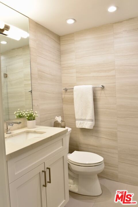 Bathroom with a white vanity, wall-mounted towel bar, and toilet against beige tile walls.