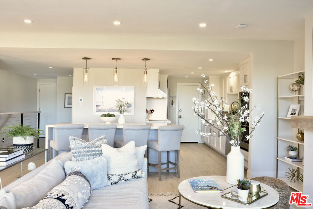 Open living and dining area with a white sofa, kitchen island, and pale wood flooring.