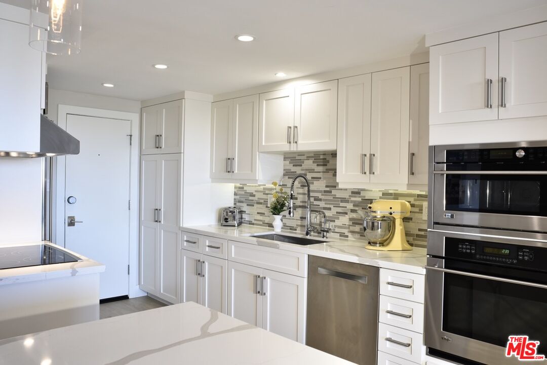 Bright white kitchen with a gray tile backsplash, stainless appliances, and a yellow stand mixer.