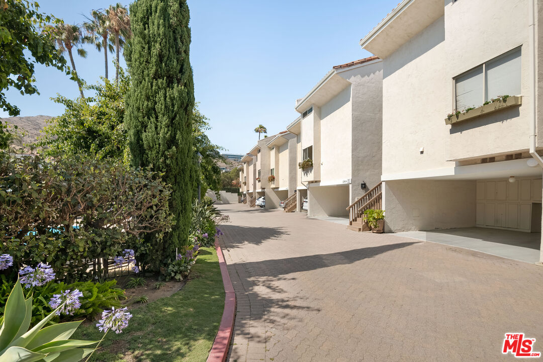 Multi-unit residential buildings along a paved driveway, with landscaped grounds and a distant hillside.