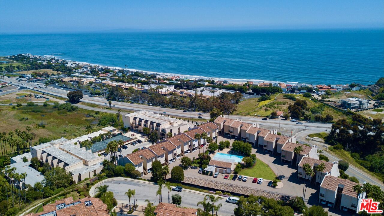 Aerial view of coastal condominium complex beside the Pacific Ocean, with a pool and shoreline.