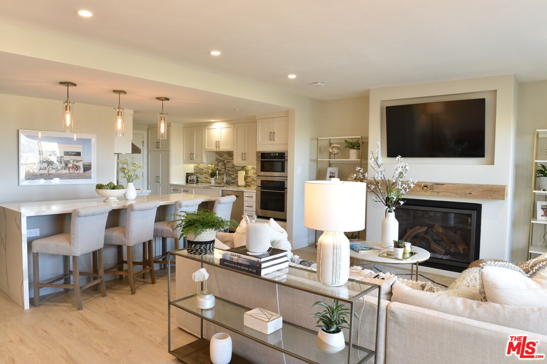 Open-plan living room and kitchen with a fireplace, breakfast bar, and light wood floors.