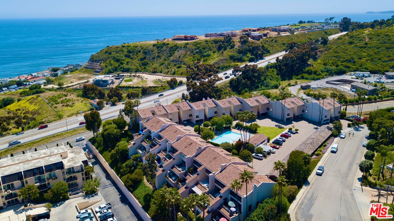 Aerial view of coastal townhomes beside the Pacific Ocean, with a swimming pool and hillside homes.