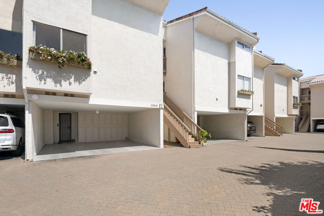Multi-unit stucco residences with exterior stairs, garage bays, and a paved courtyard.
