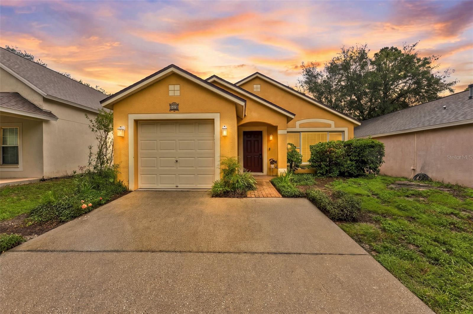 Yellow stucco home with a single garage and brick entry walk at sunset.