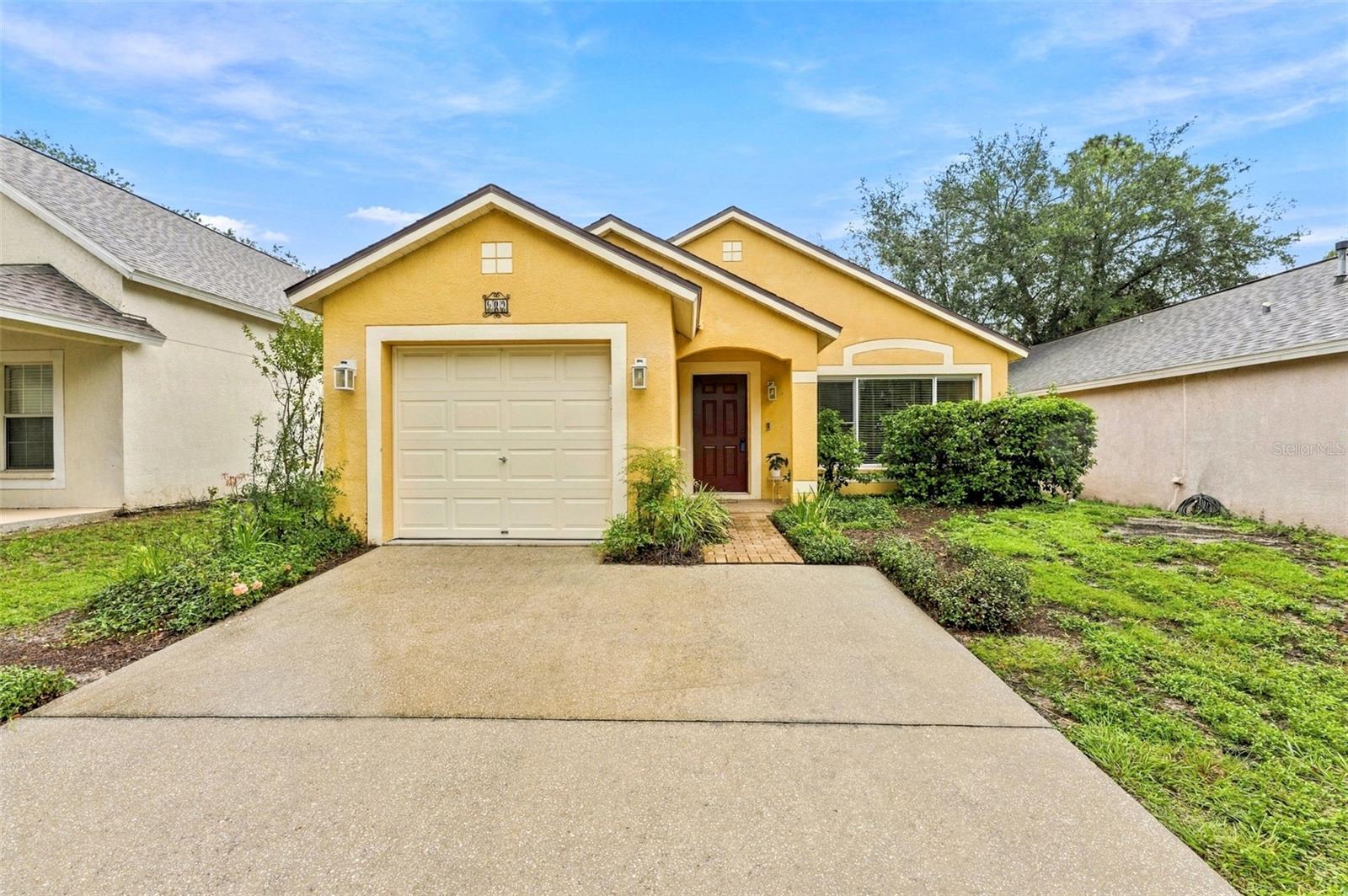 Yellow stucco home with a single-car garage, paved driveway, and landscaped front yard.