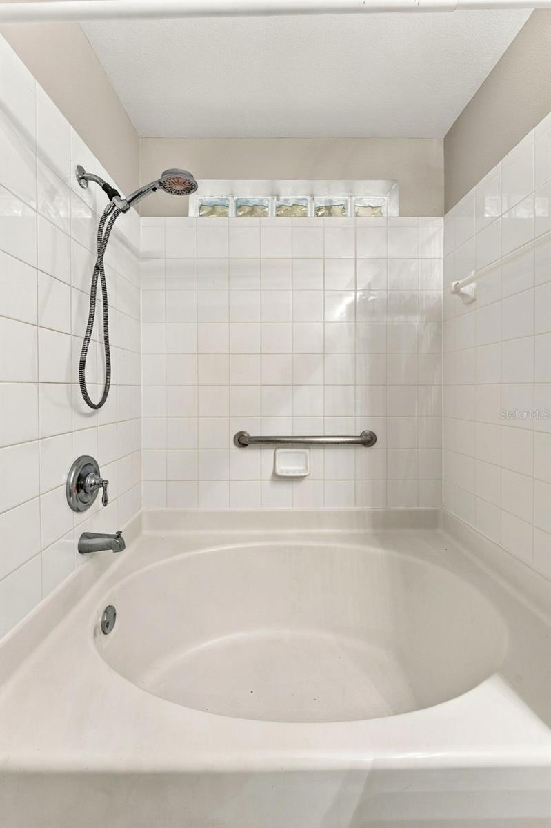 White bathtub and tiled shower with a handheld showerhead and grab bar.