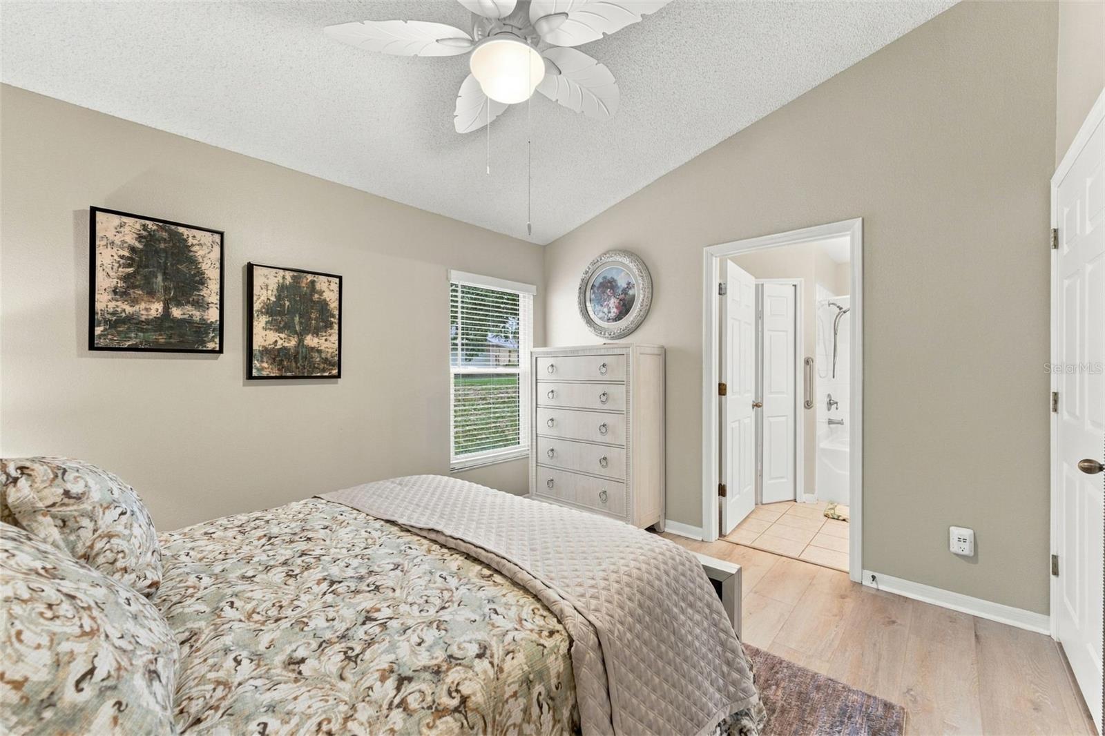Bedroom with a patterned bed, ceiling fan, and doorway to an adjoining bathroom.