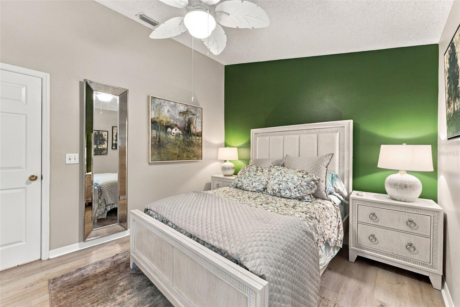 Bedroom with a white upholstered bed, green accent wall, matching nightstands, and ceiling fan.