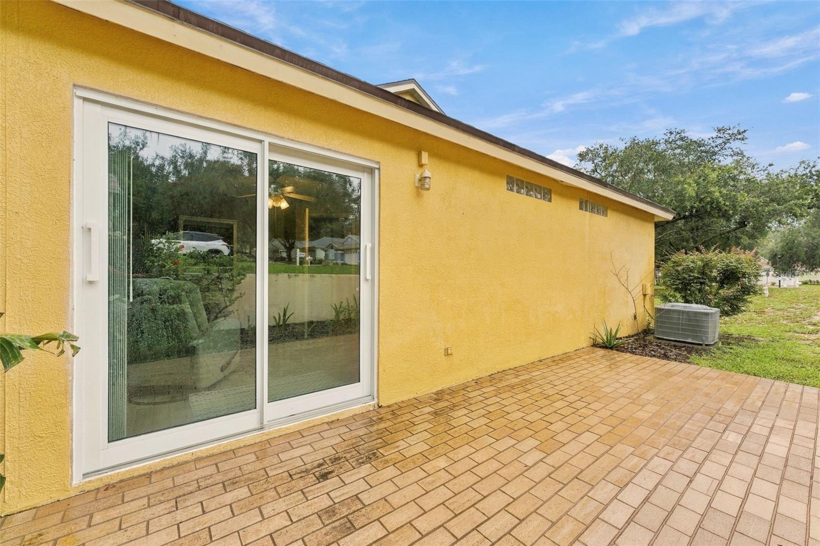 Yellow stucco home exterior with a sliding glass door opening onto a brick-paver patio.