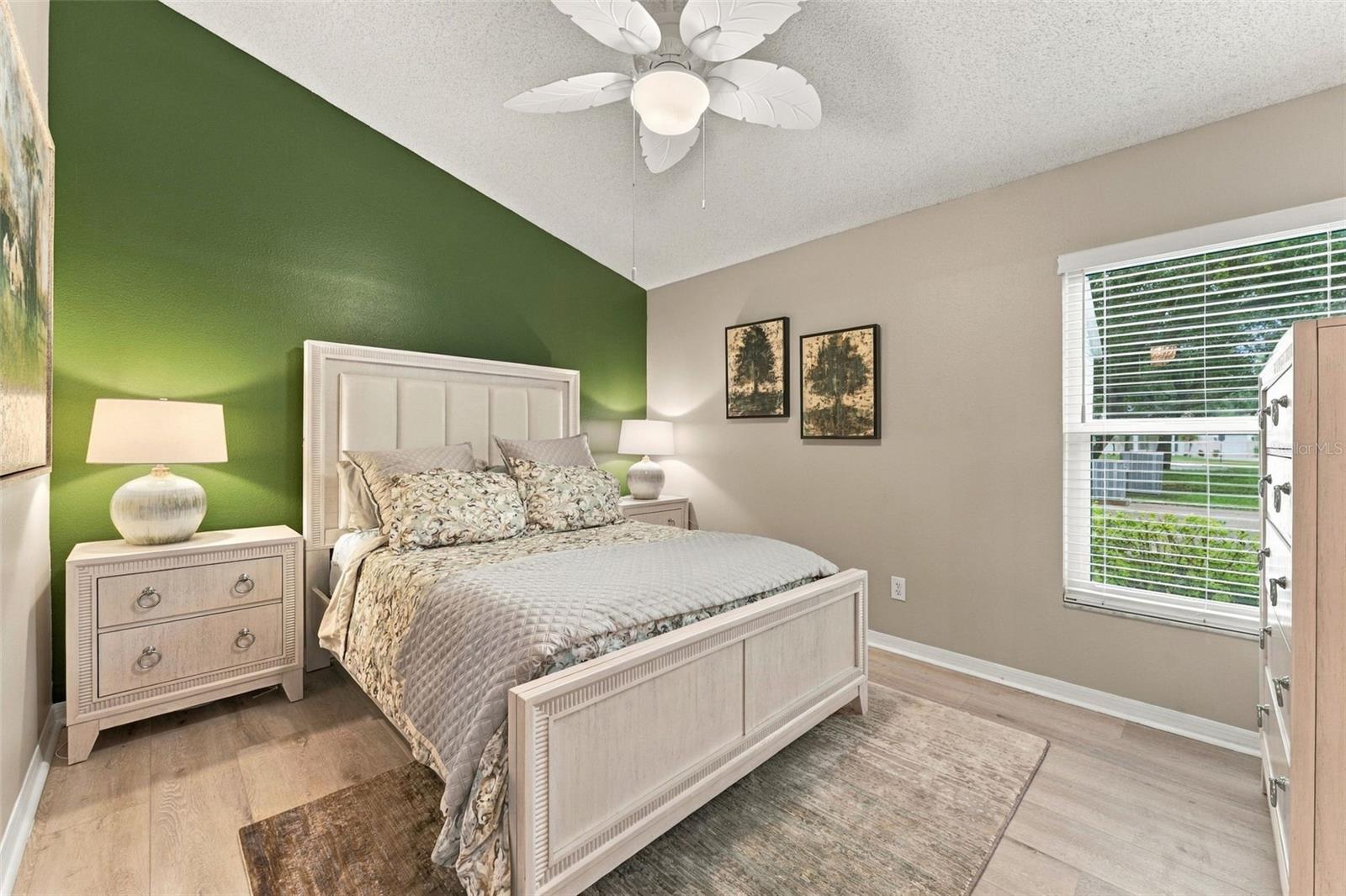 Bedroom with a white bed against a green accent wall and a window with white blinds.