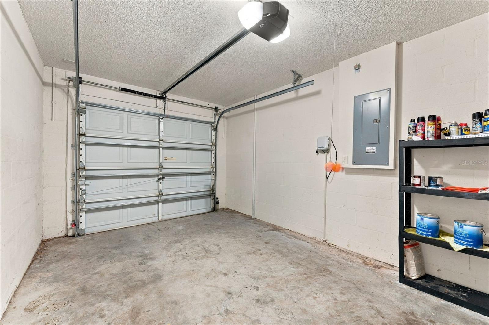 Garage with a closed sectional door, concrete floor, and wall-mounted storage shelf.