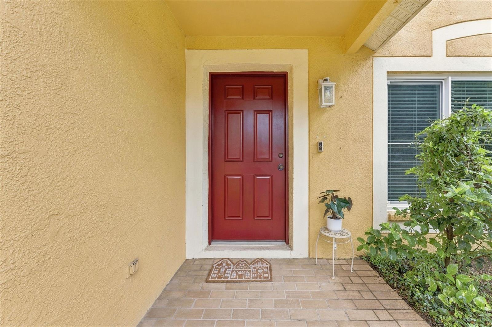 Home's covered front entry with a red paneled door, tiled porch, and potted plant.