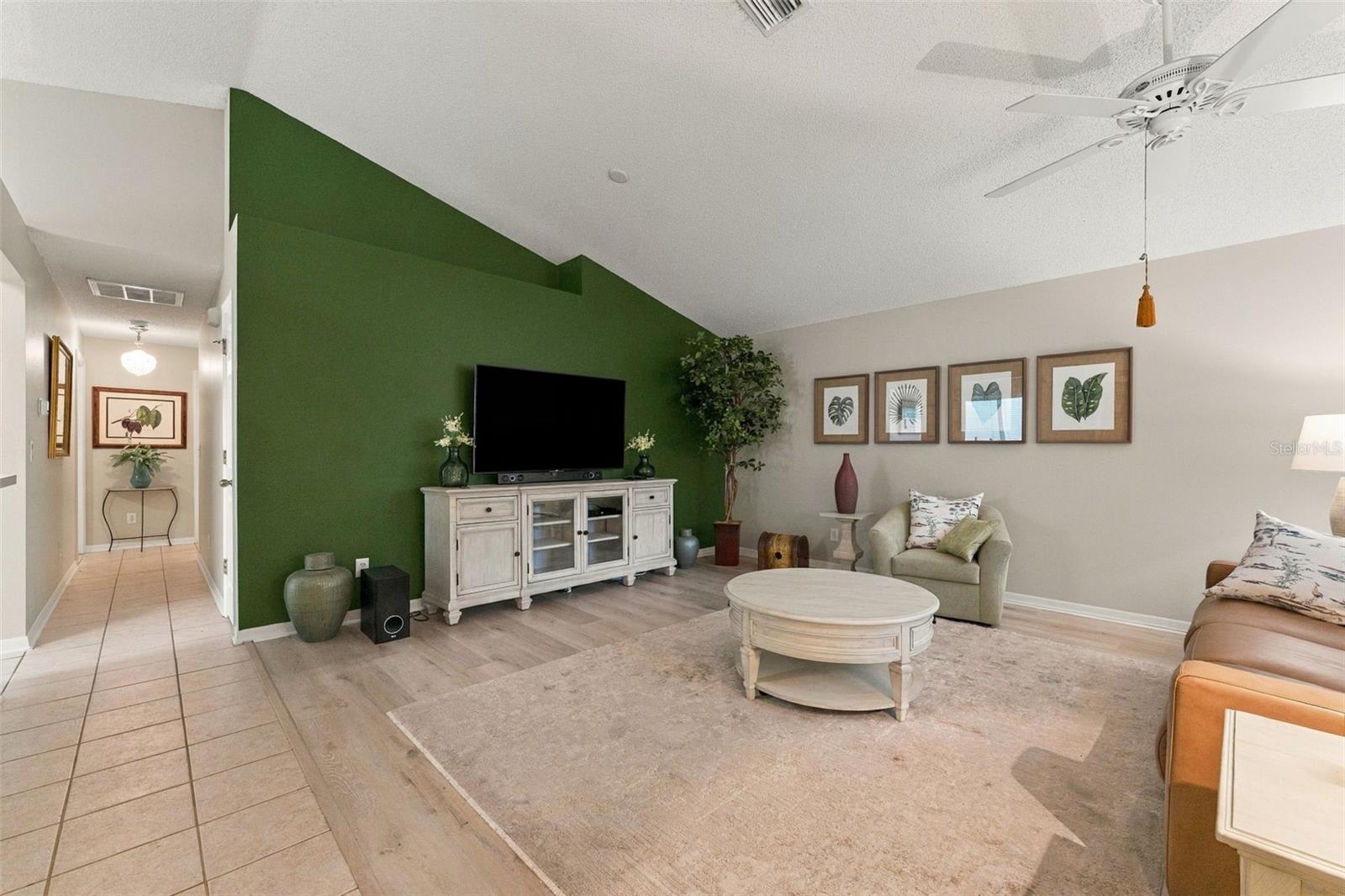 Living room with a green accent wall, media console, and neutral seating.