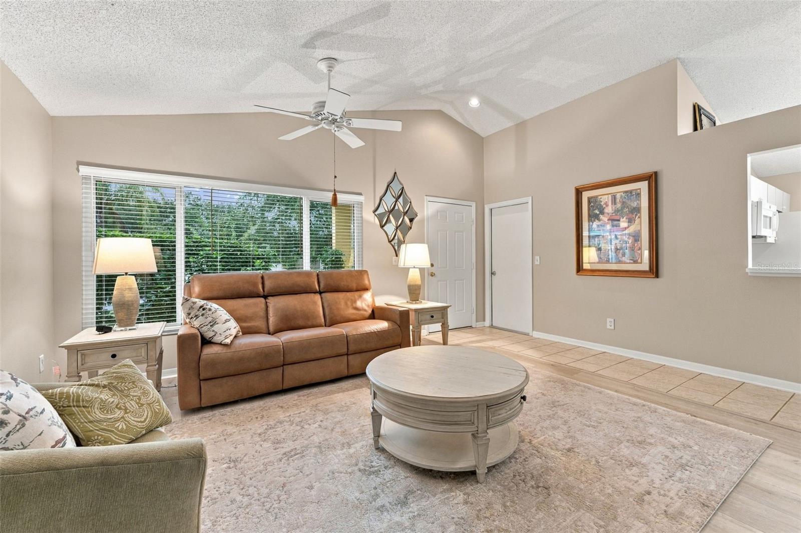 Living room with a brown leather sofa, round coffee table, and large windows with blinds.