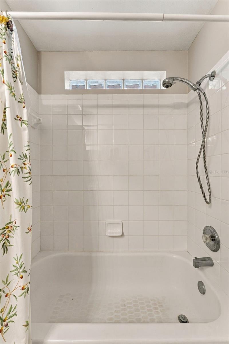 Bathroom tub and tiled shower with a handheld showerhead and floral curtain.