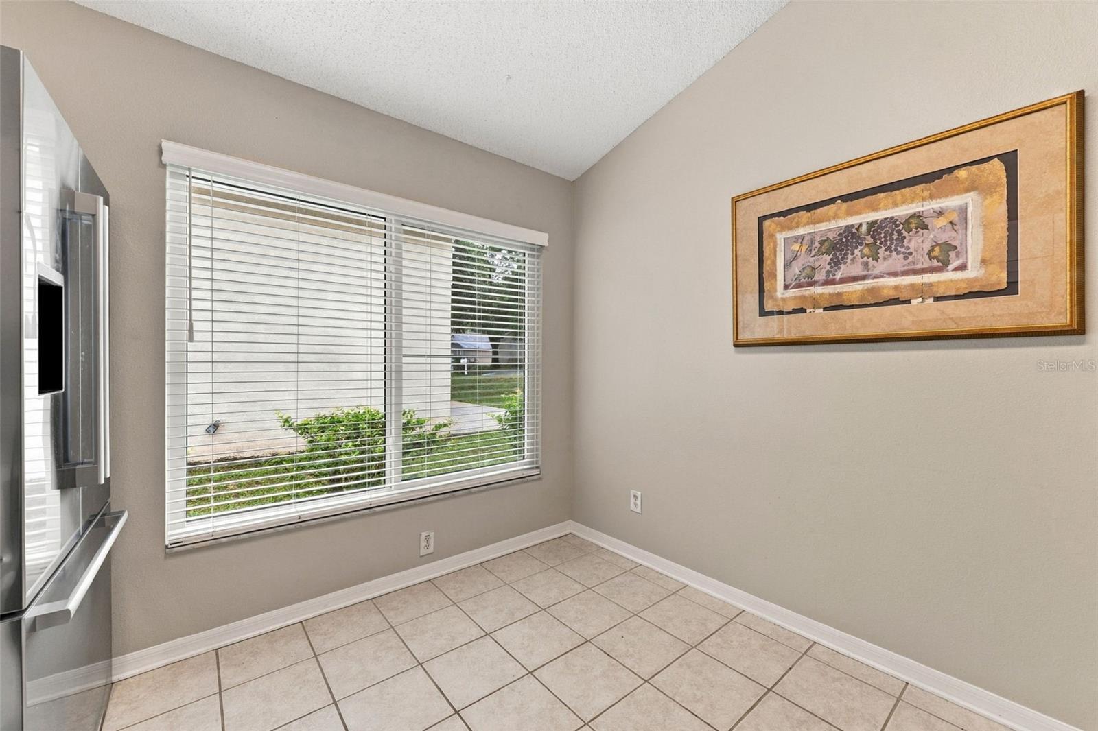 Tiled interior room with a large window, white blinds, framed artwork, and a television at the edge.