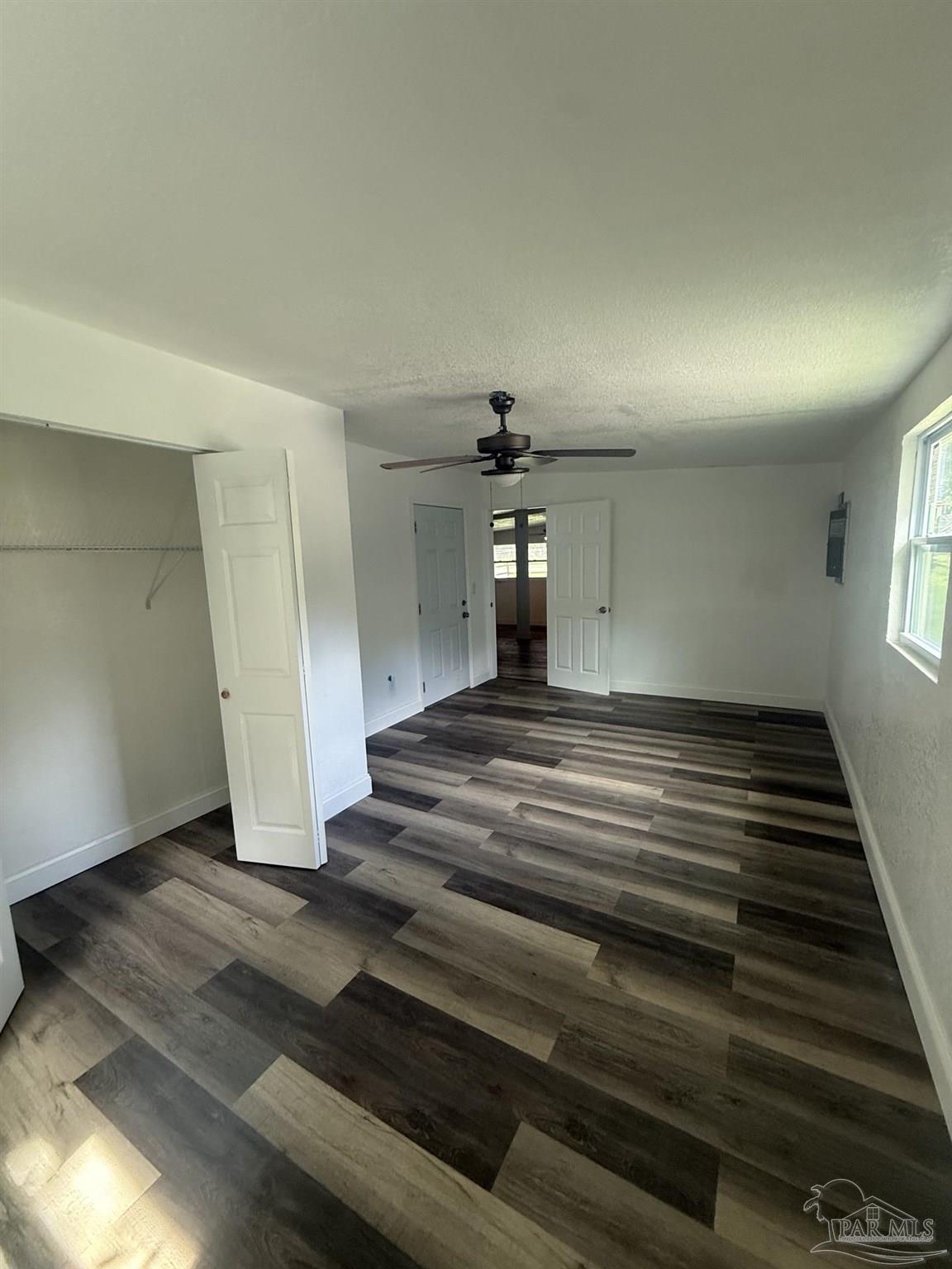 Empty bedroom with multitone plank flooring, a ceiling fan, and an open closet.