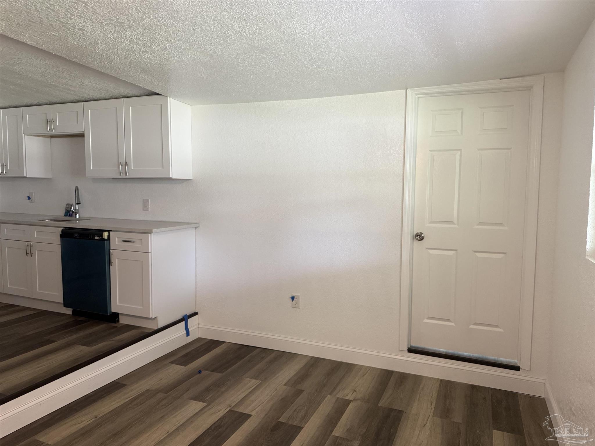 Small kitchen with white cabinets, dark dishwasher, wood-look flooring, and a raised step.