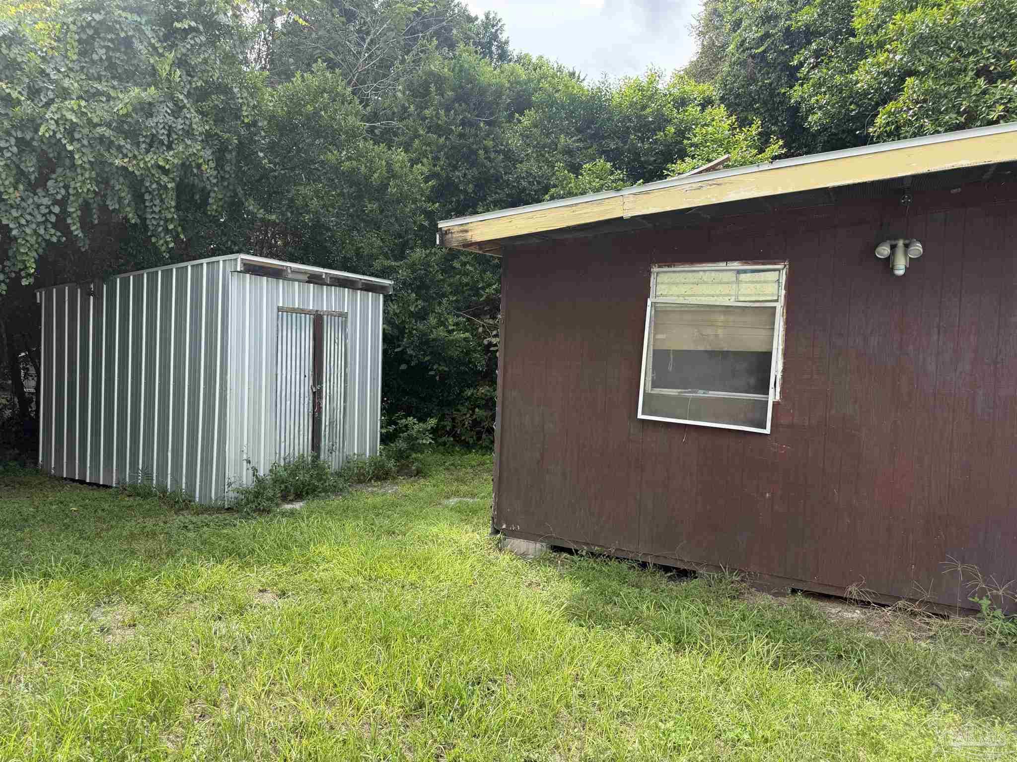 Brown outbuilding and corrugated metal shed in a grassy, wooded yard.