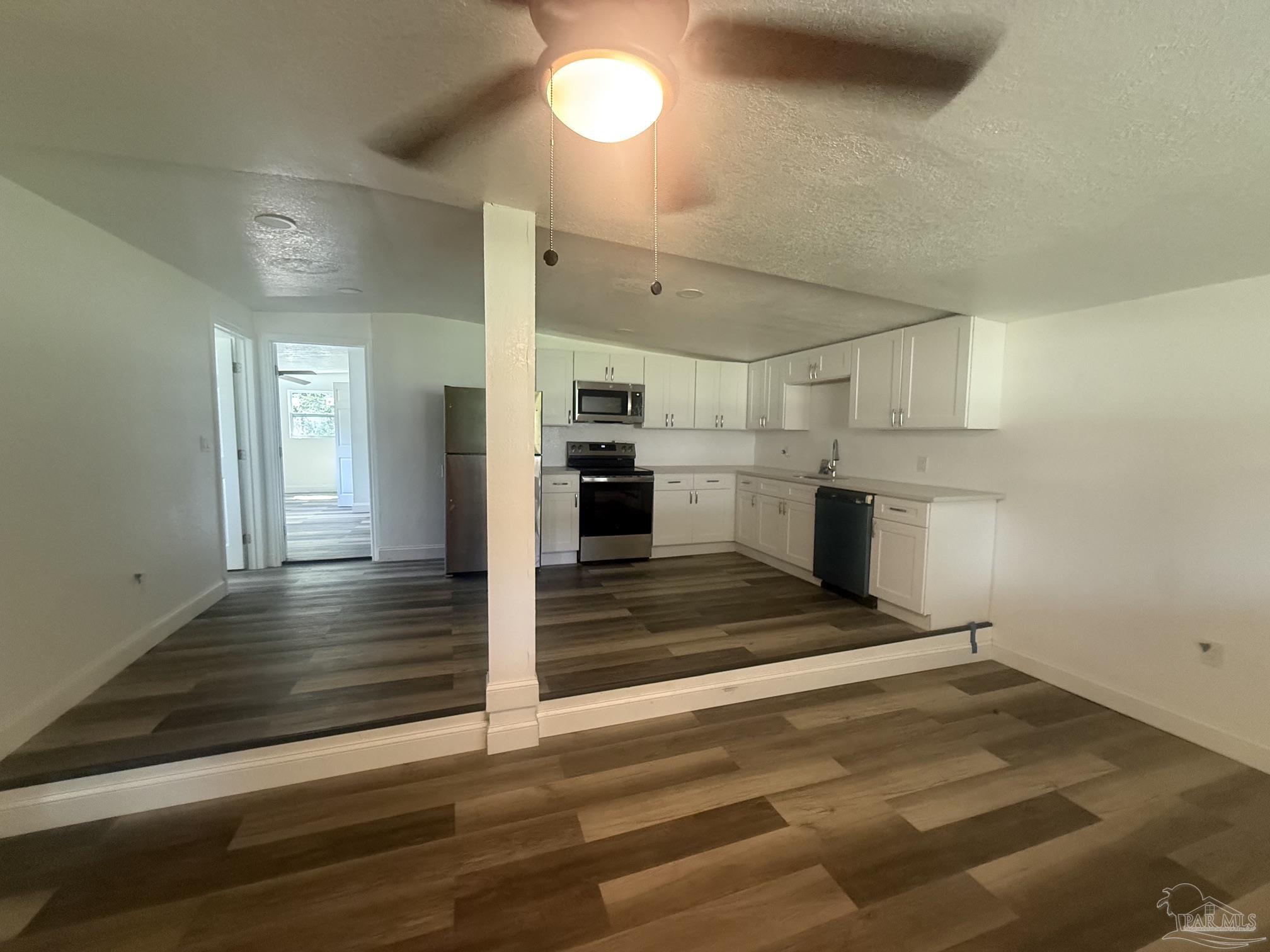 Open kitchen with white cabinets, stainless steel appliances, and brown wood-look flooring.