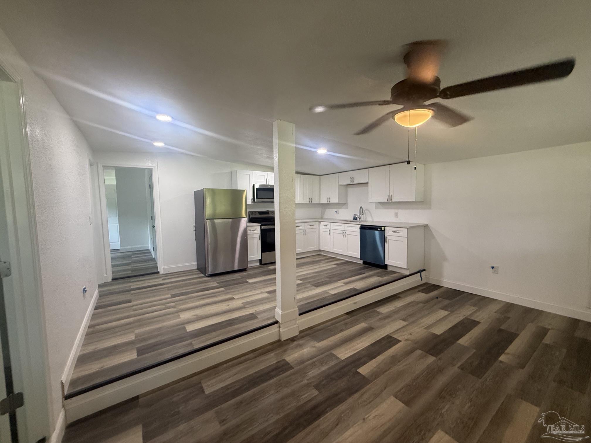 Vacant kitchen with white cabinets, stainless steel appliances, and gray wood-look flooring.