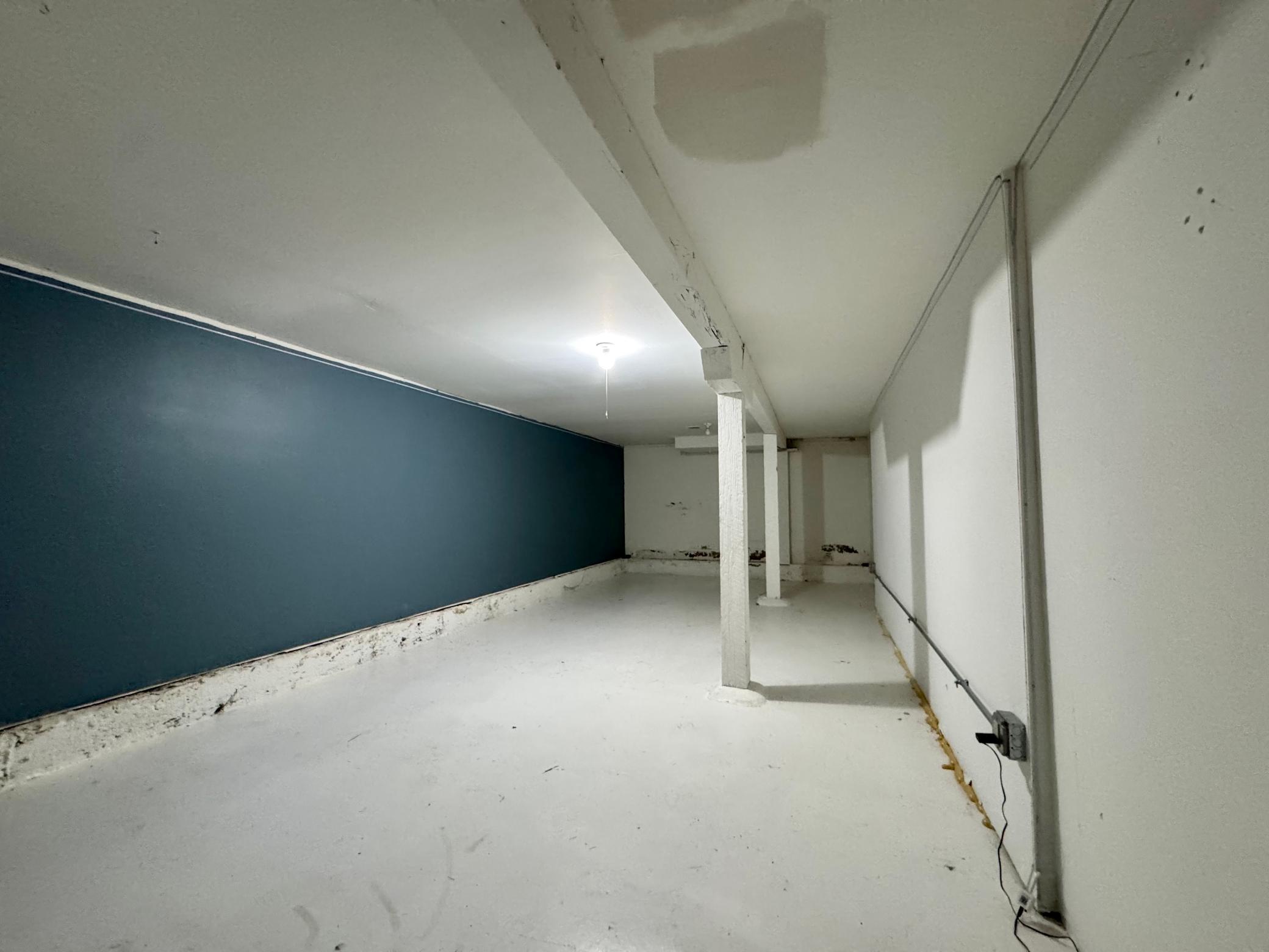 Unfinished basement with a dark blue wall, white floor, and support posts.