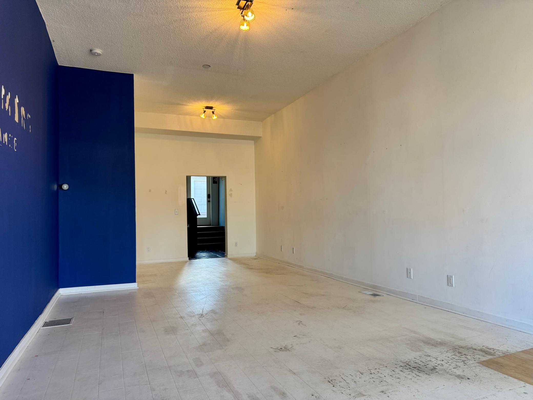 Vacant tiled room with a deep blue accent wall and doorway to stairs