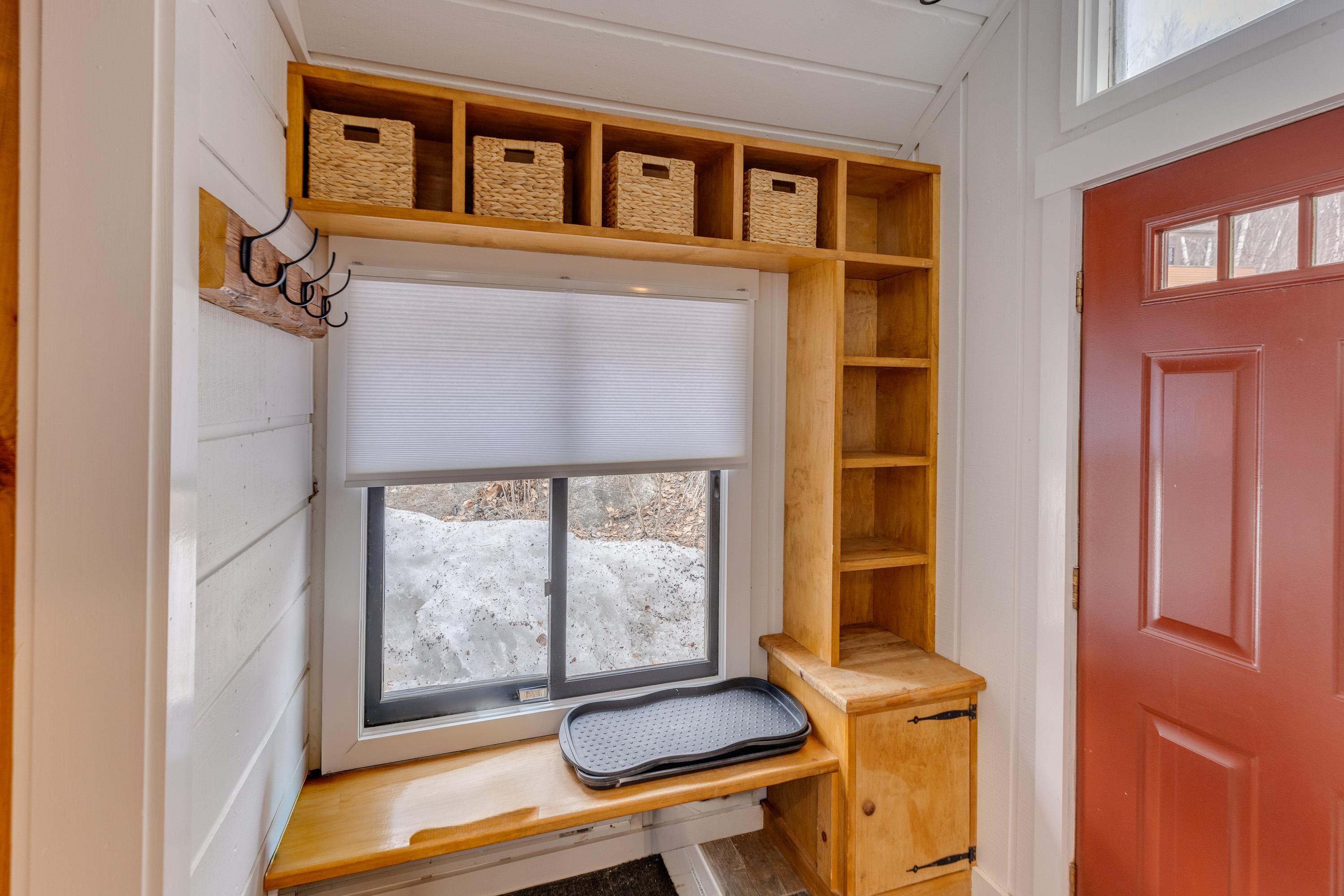 Mudroom entry with wooden built-in cubbies, bench, coat hooks, snowy window, and red door.