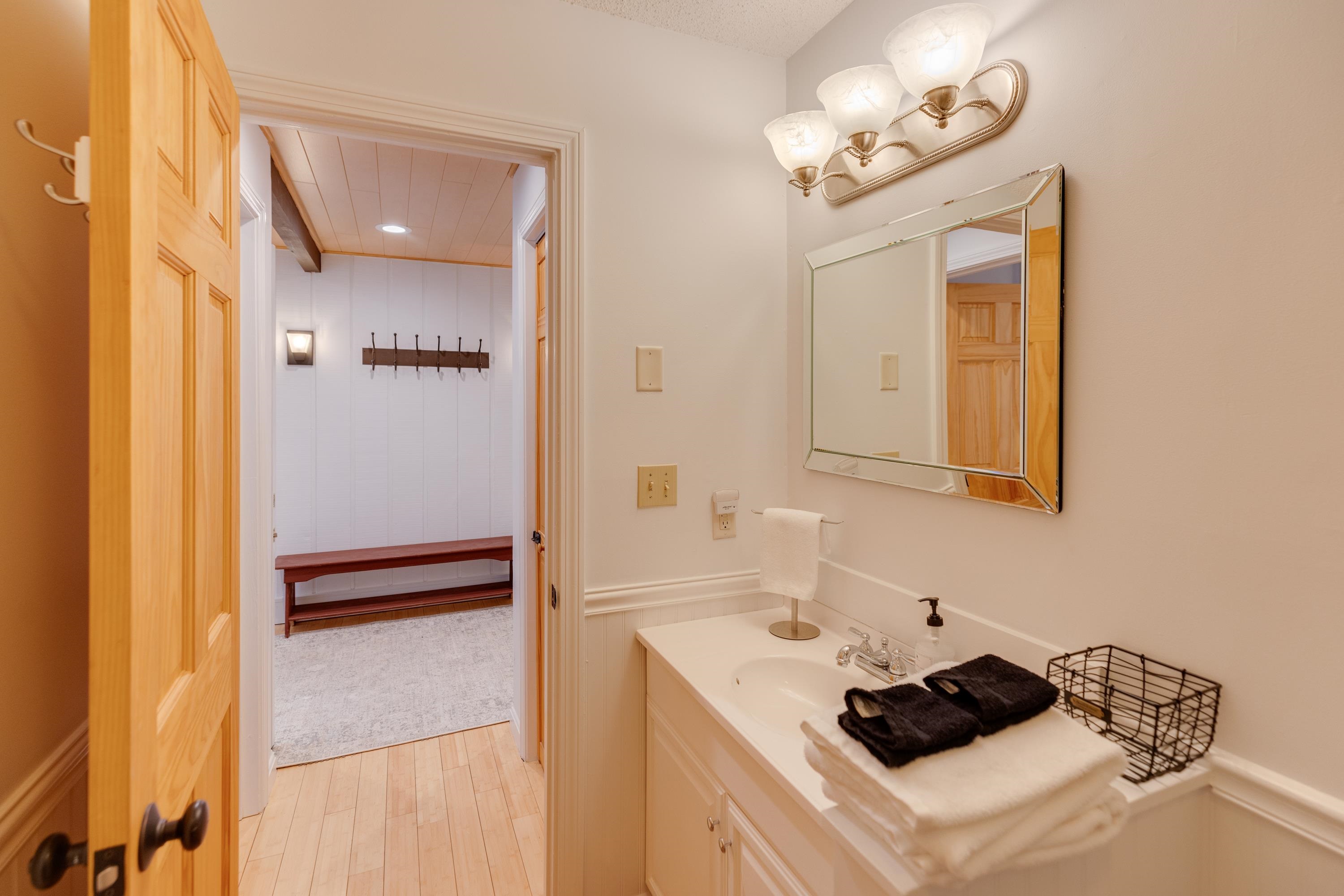 Bathroom vanity and mirror beside an open doorway to an entry bench and wall hooks.