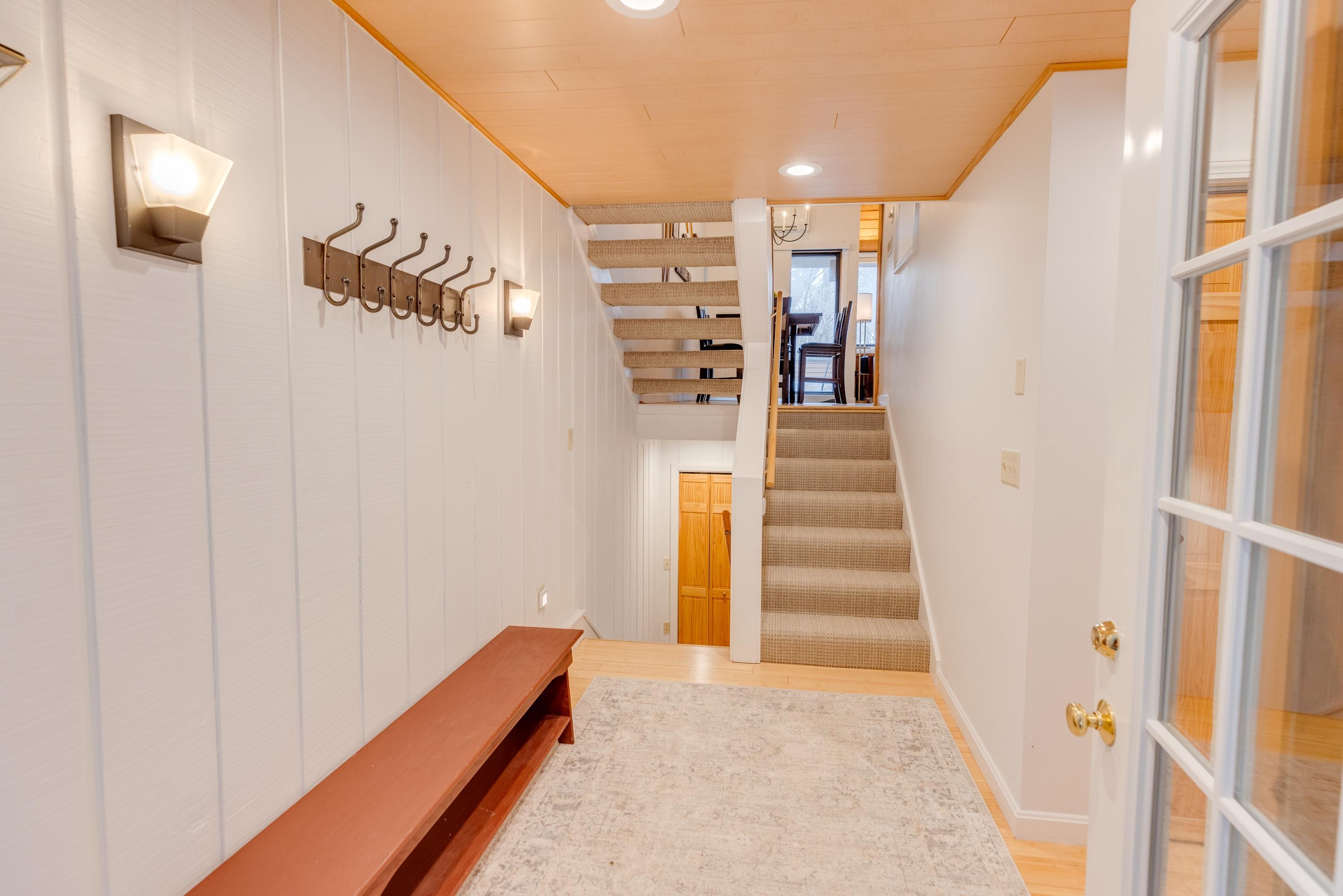 Entry hall with a wooden bench, wall hooks, and carpeted stairs leading to a dining area.