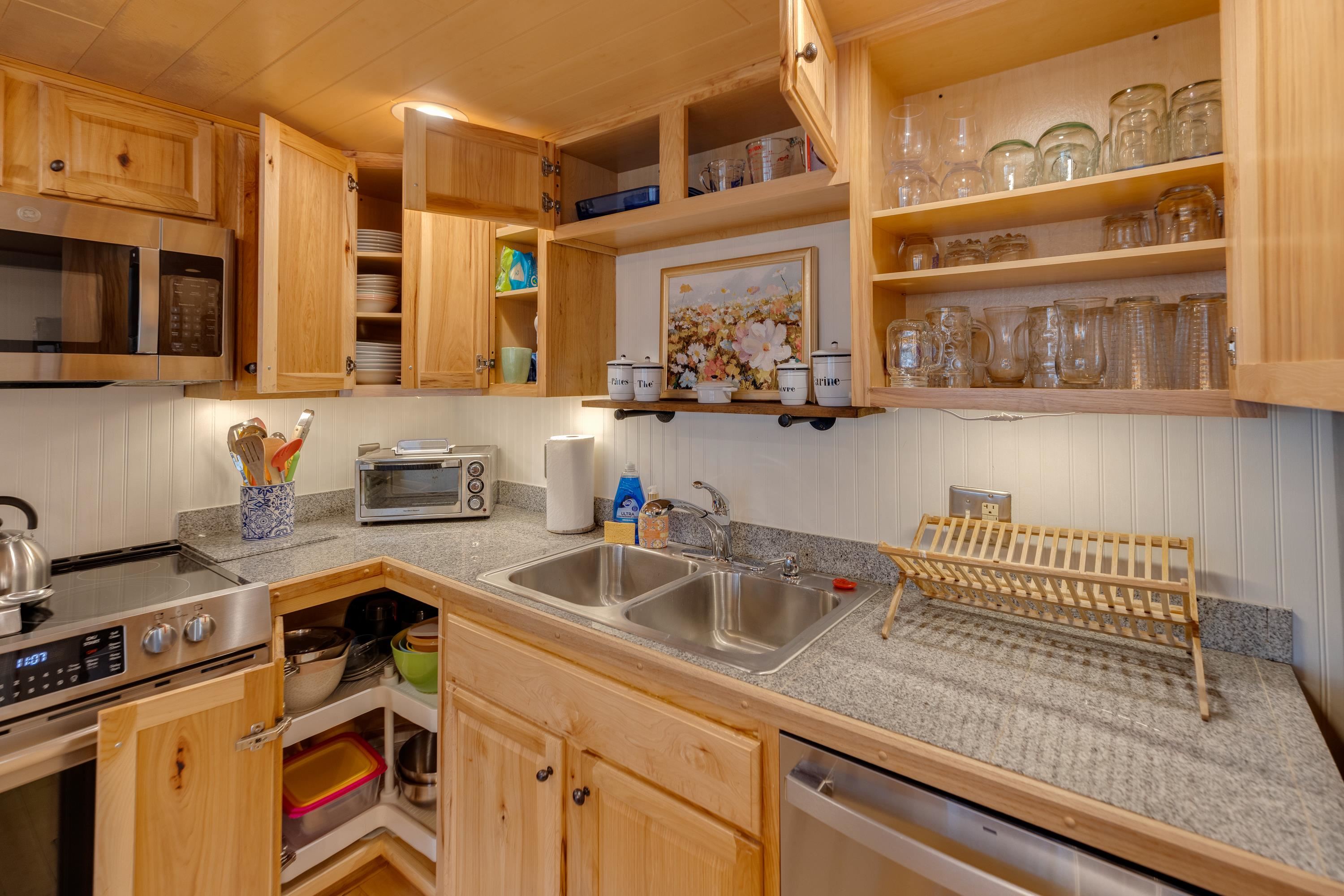 Compact kitchen with open light-wood cabinets, granite counters, and a double-basin sink.