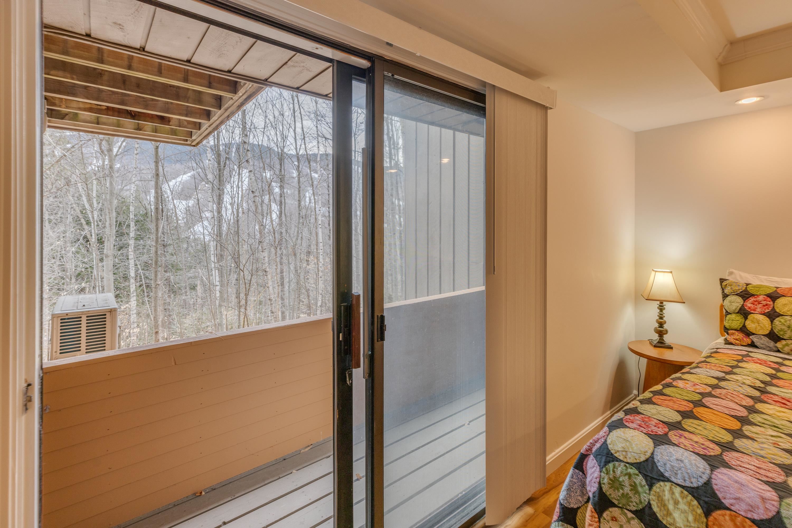 Bedroom with a colorful quilt and sliding glass doors to a covered balcony overlooking leafless woods.