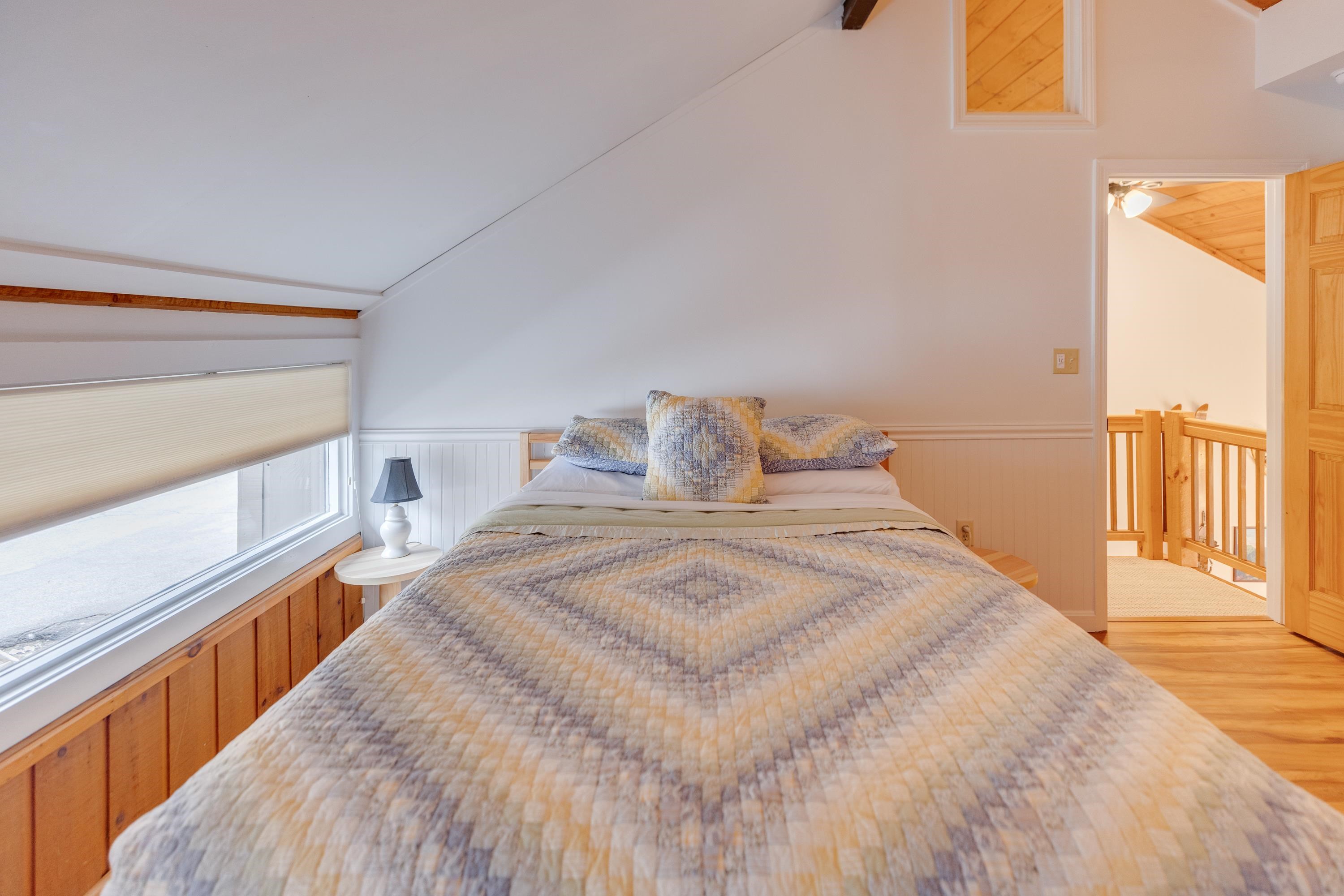 Furnished bedroom with a large patterned bed, long window, and doorway to a wood-railed landing.