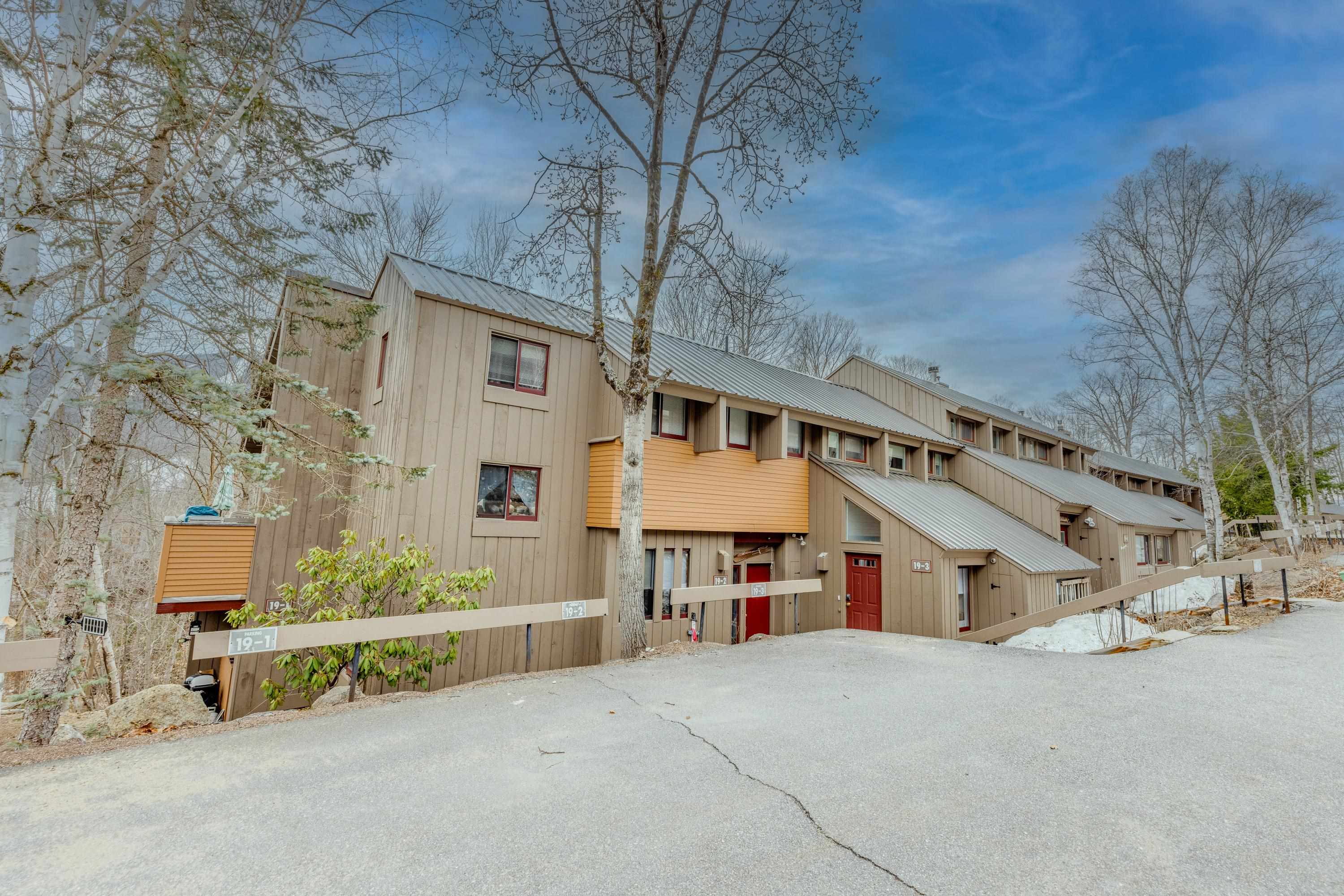 Townhouse-style condominium exterior with tan siding, red doors, and unit 19-3 marked by the entrance.