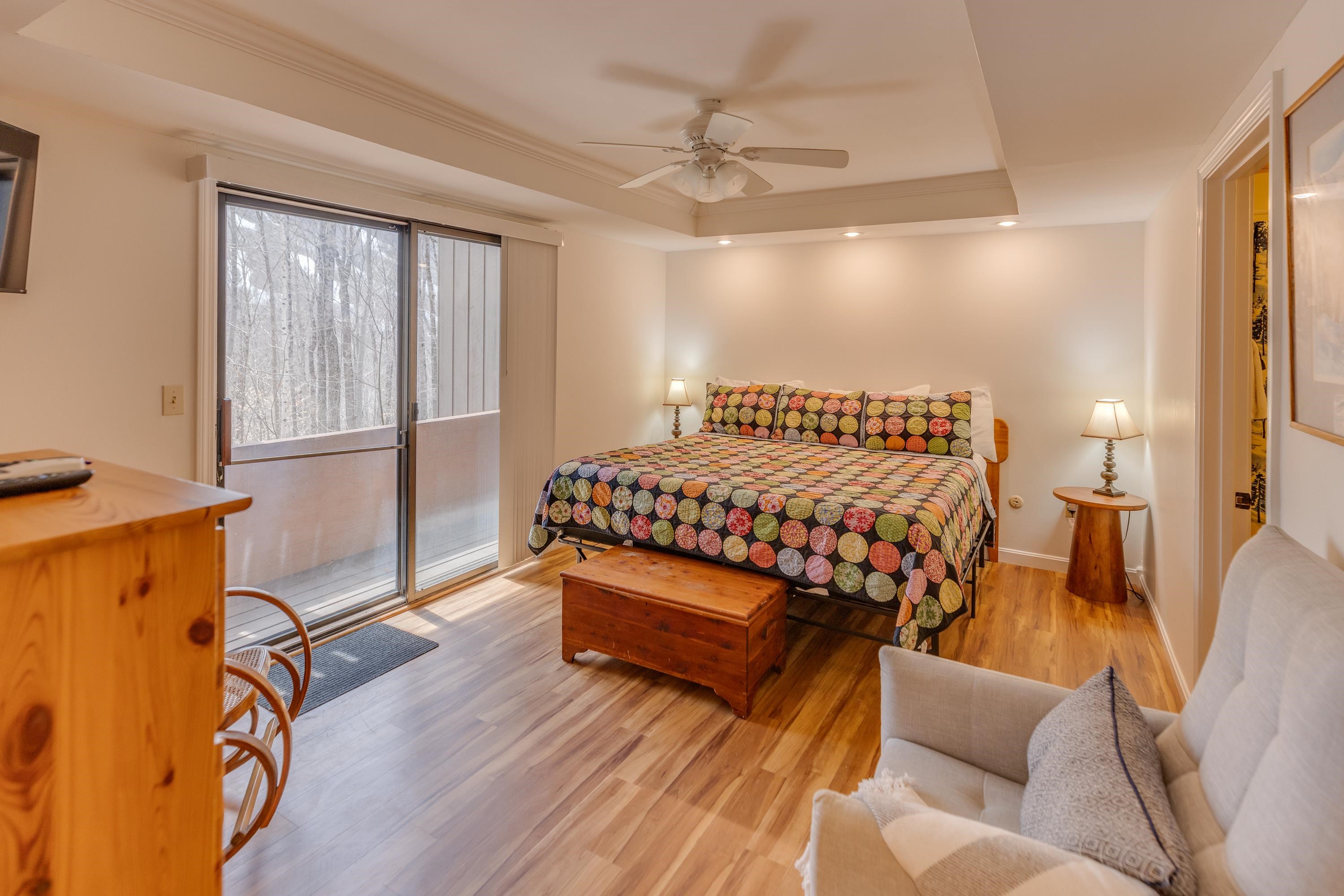 Furnished bedroom with a colorful quilted bed and sliding doors overlooking the woods.